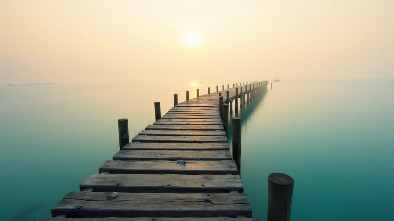 A weathered wooden pier stretching into calm misty sea at early morning